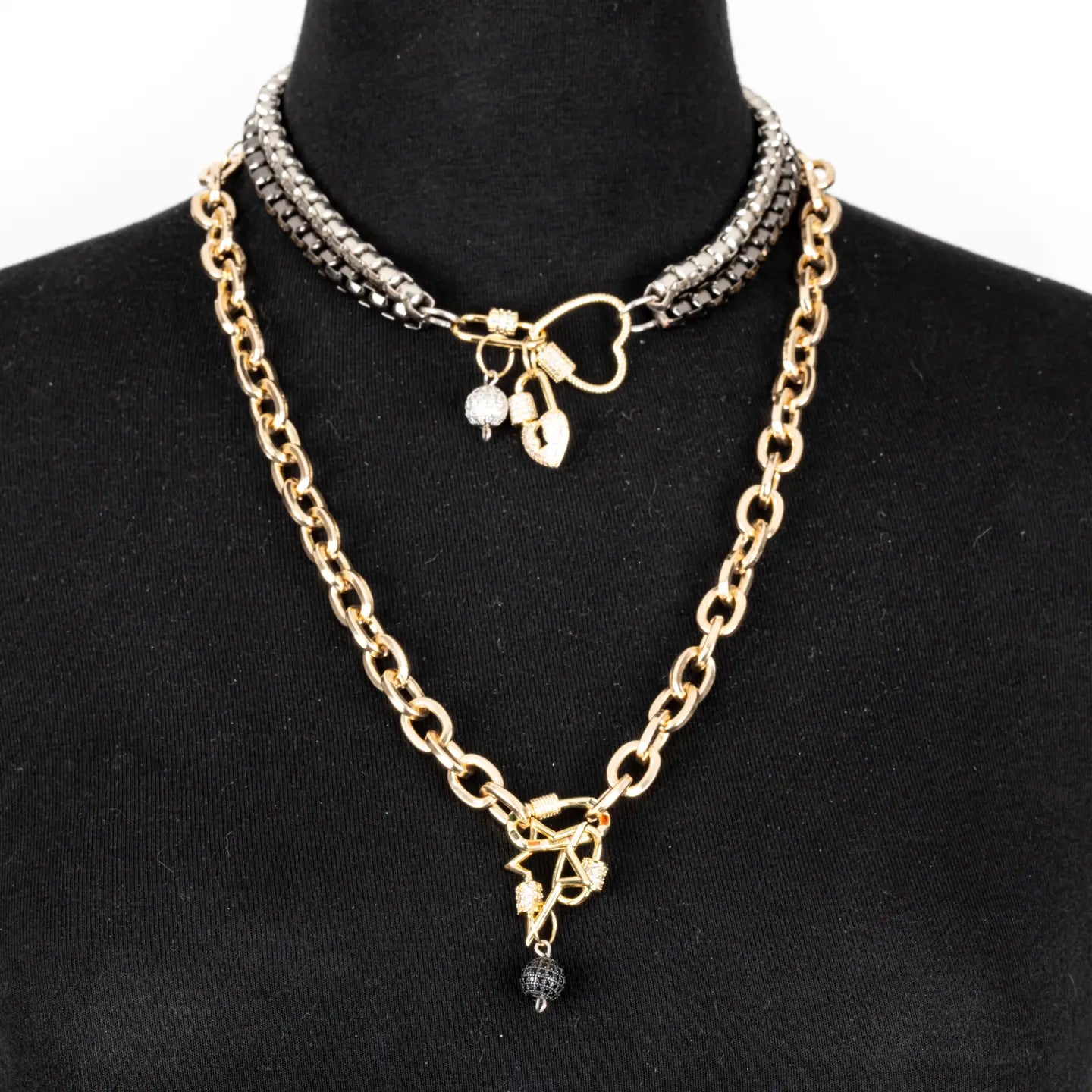 Mixed metal necklace with heart connector, charm details, and drop chain in gold and gunmetal tones on white background.