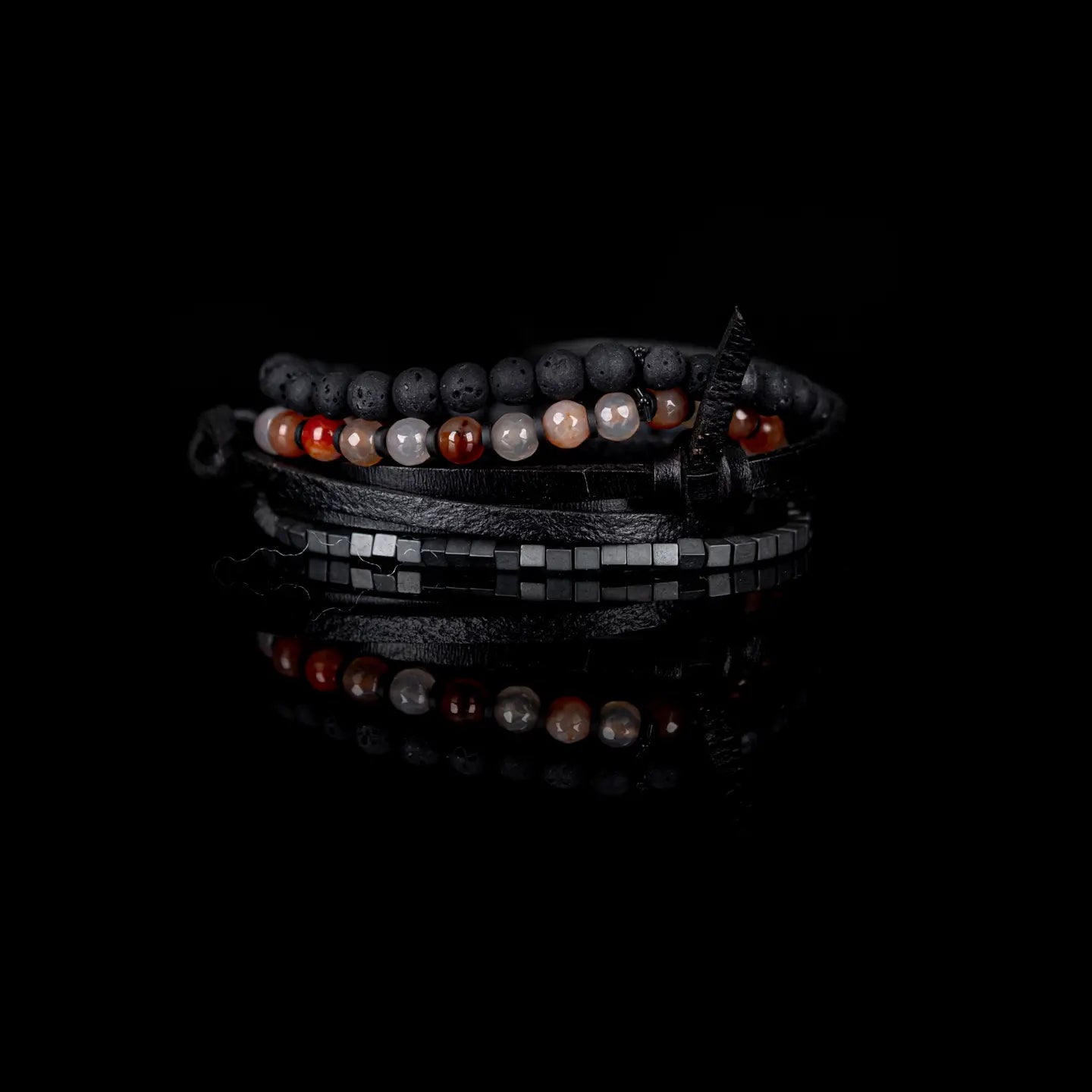 Men's layered bracelet set featuring matte black lava stone beads, faceted brown and cream agate gemstone beads, dark hematite cube beads, and black leather wrap straps arranged in a handcrafted stacked design on a white background.