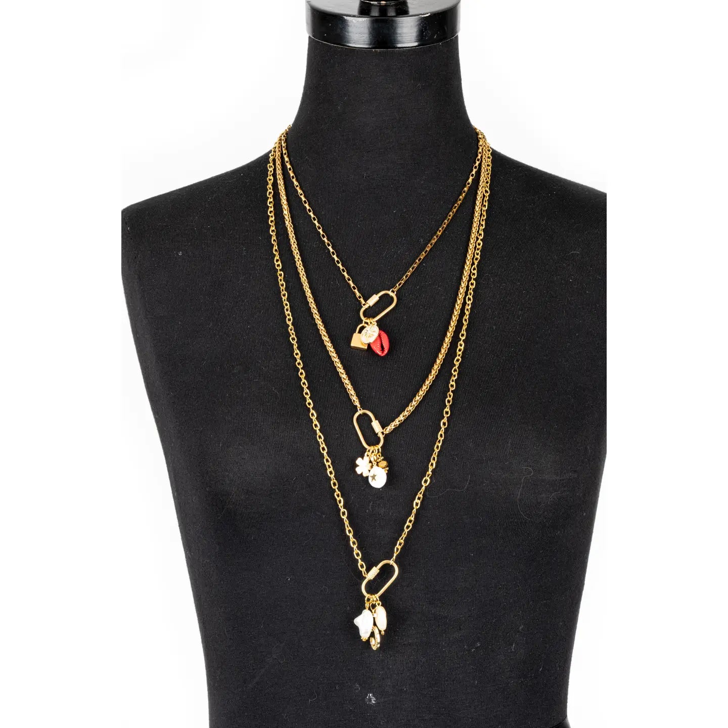 Layered gold necklace with three chains and small charm details on white background.