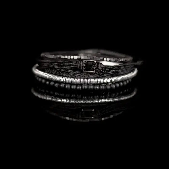 Black and silver layered men’s bracelet set with matte black beads, silver hematite-style spacers, braided rope wraps, and minimalist metallic centerpiece on white background.