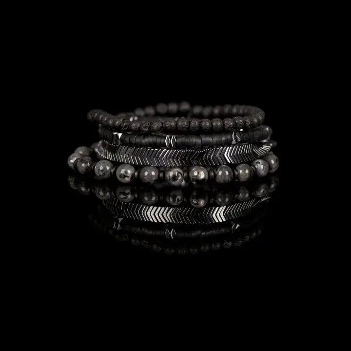 Black and silver multi-layer men’s bracelet featuring lava stone beads, hematite disc strands, silver chevron metal detail, pyramid-cut metallic accents, and marble grey natural stone beads on a light background.