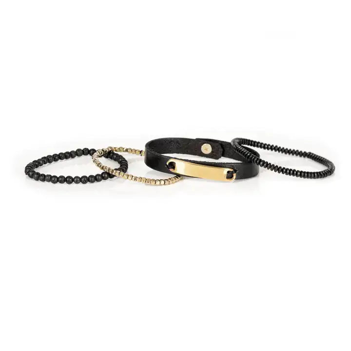 Men’s layered bracelet set featuring a black leather cuff with a polished gold-tone ID plate, matte black lava stone beads, gold-tone hematite spacer beads, and black heishi beads, stacked in a sophisticated black and gold luxury design on a white background.