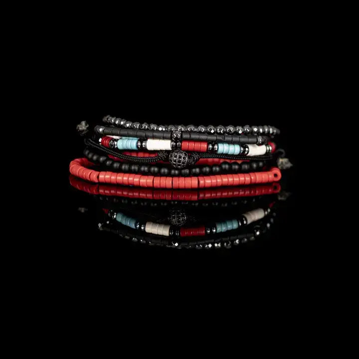 Men’s layered bracelet set featuring faceted hematite crystal beads, black heishi beads, turquoise and coral-red accent beads, matte black bead strands, black braided cord wraps, and a pavé-style gunmetal centerpiece, stacked in a bold contemporary bohemian luxury design on a white background.