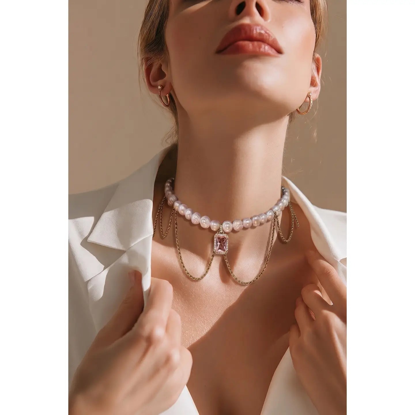 Pearl necklace with draped gold chains and a pink crystal pendant on a white background.
