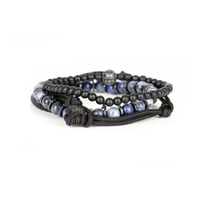 Black and blue layered men’s bracelet set with matte black beads, blue marbled stone accents, braided rope wraps, and pavé centerpiece on white background.