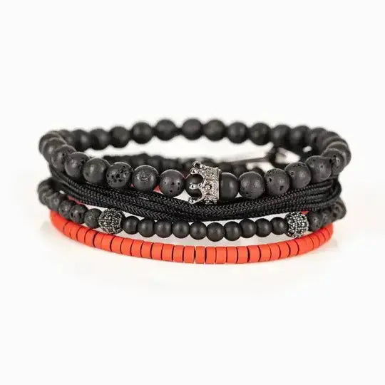 Men’s layered bracelet set featuring matte black lava stone beads, black braided cord, black onyx-style beads, gunmetal accent beads, a crown charm centerpiece, and vibrant red heishi beads, stacked in a bold contemporary luxury design on a white background.
