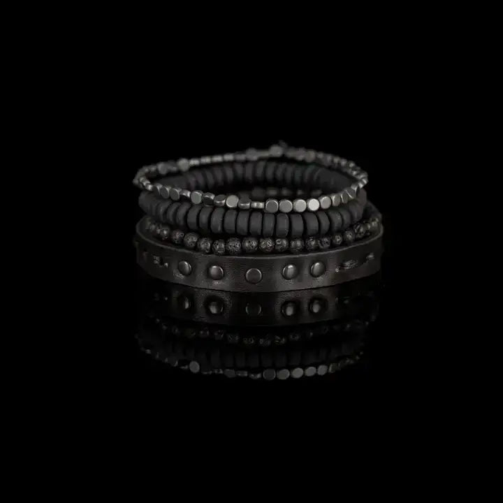 Black multi-layer men’s bracelet set featuring studded leather band, matte onyx beads, lava stone, faceted hematite accents, and layered black beaded strands on a light background.