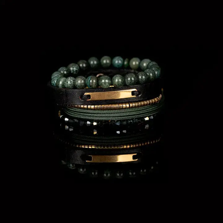 Men’s layered bracelet set featuring green natural stone beads, a black leather cuff with a gold-tone ID plate, olive braided cord wraps, gold-tone heishi beads, and faceted green crystal beads, stacked in a refined earthy luxury design on a white background.