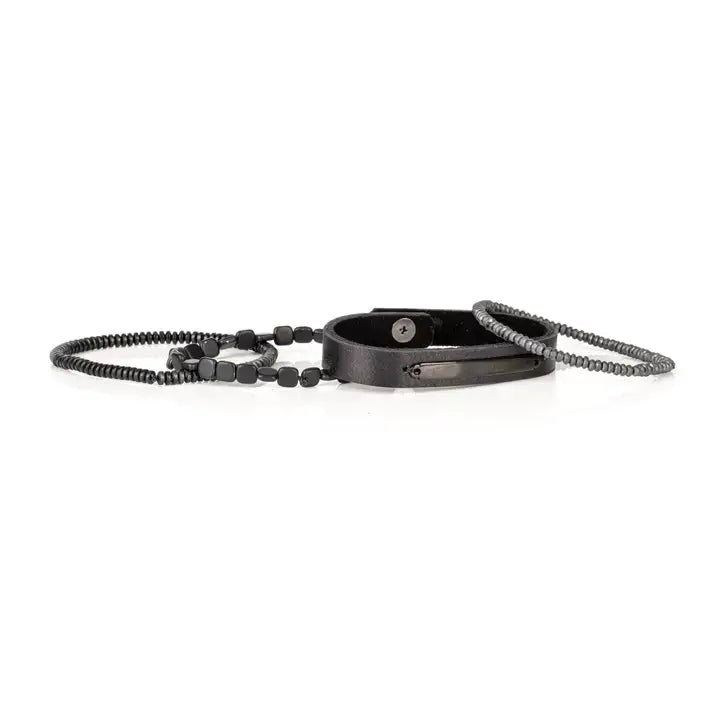 Black multi-layer men’s bracelet set featuring matte onyx beads, braided black rope, crystal cross centerpiece, gold chevron metal bar, and layered metallic accents on a light background.