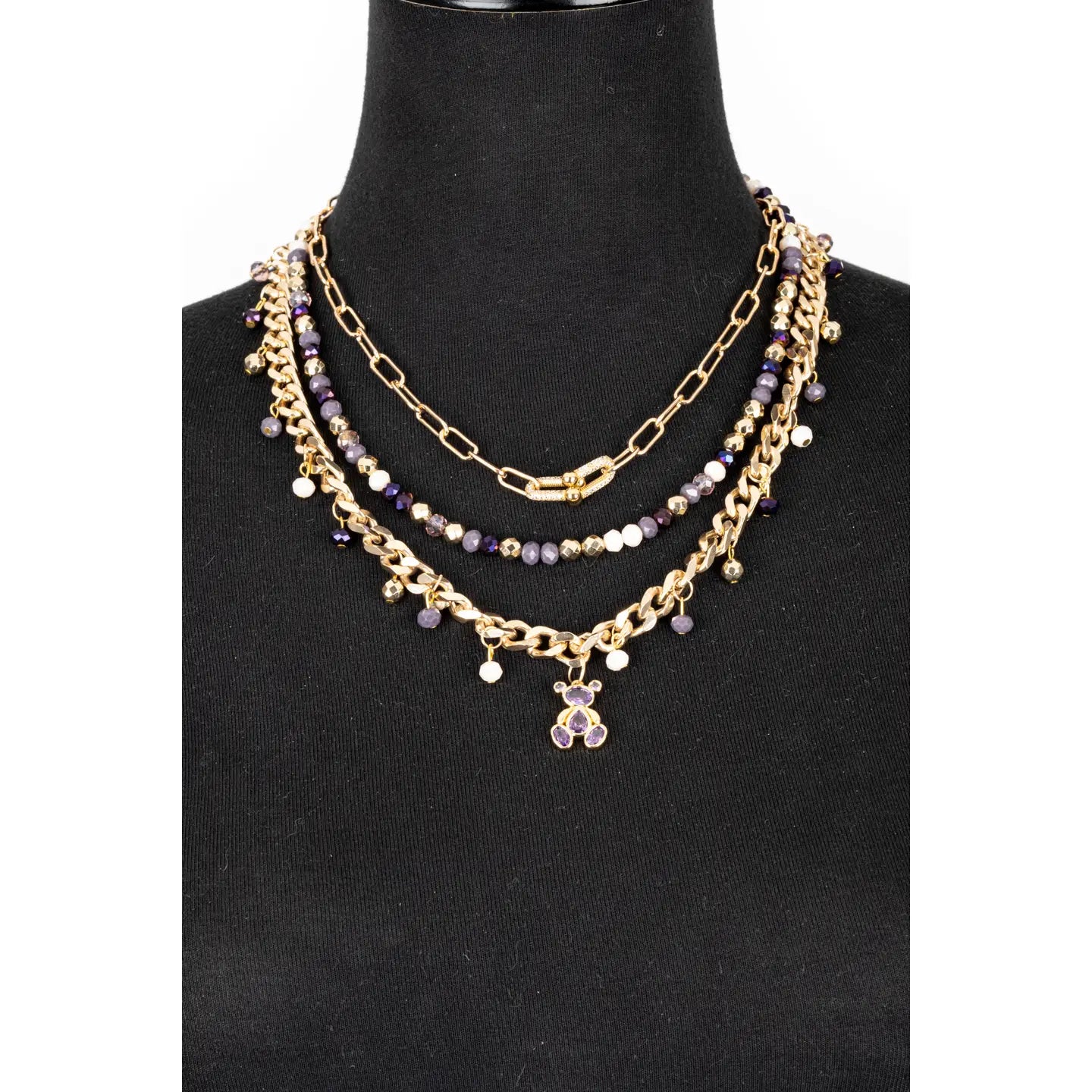 Layered gold necklace with purple crystal beads and small bear charm on white background.