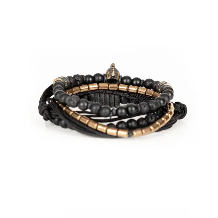 Black layered men’s bracelet set with lava stone beads, metallic skull centerpiece, gold-tone spacer accents, matte black beads, and braided rope wraps on white background.