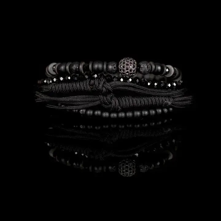 Black layered men’s bracelet set with matte black beads, faceted crystal accents, braided rope wraps, and pavé centerpiece bead on white background.