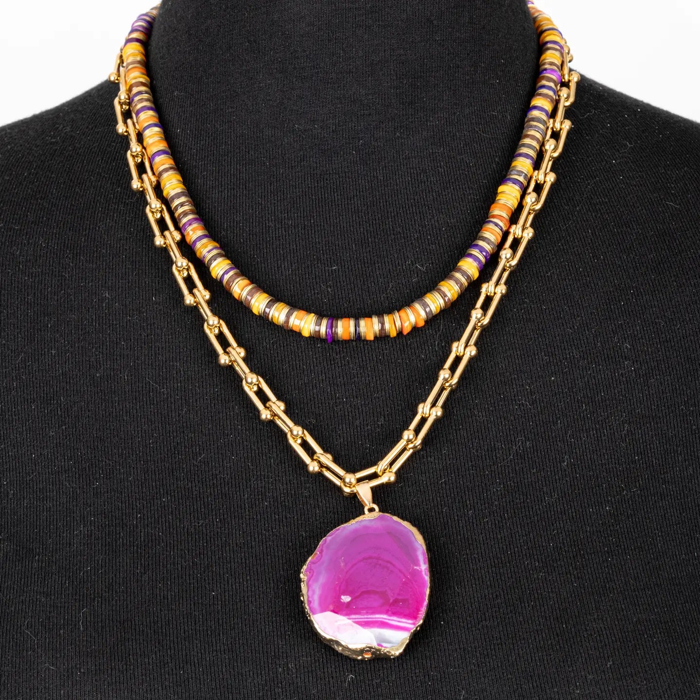 Layered necklace with multicolor beads and pink agate pendant on gold chain on white background.