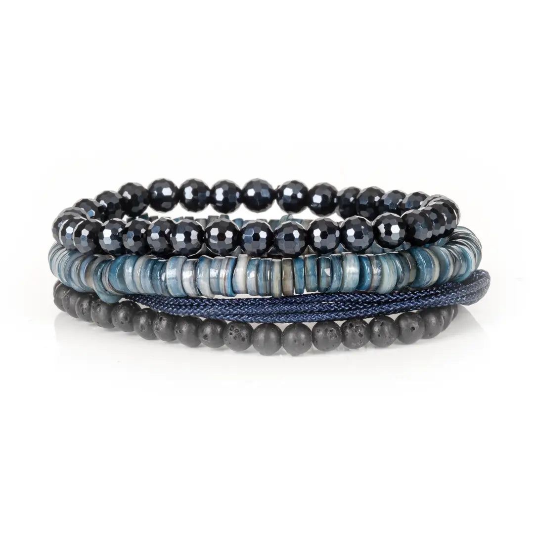 Men's layered bracelet set featuring faceted black crystal beads, blue heishi stone beads, navy woven cord, and matte black lava stone beads arranged in a stacked design on a white background.
