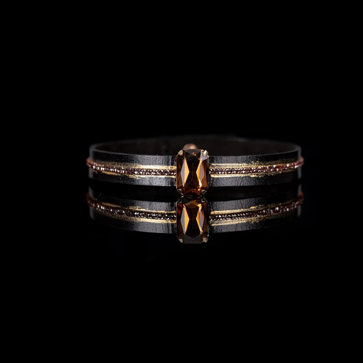 Black leather choker with a central brown rectangular crystal and fine rhinestone and gold detailing along the band, displayed on a white background.