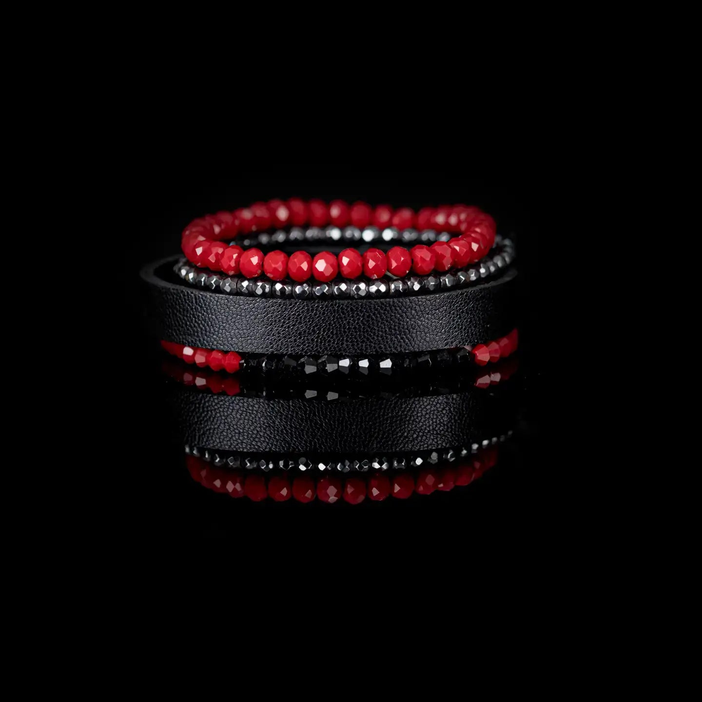 Red and black multi-layer men’s bracelet featuring faceted red crystal beads, hematite bead strands, black leather band, and black faceted stone accents on a light background.