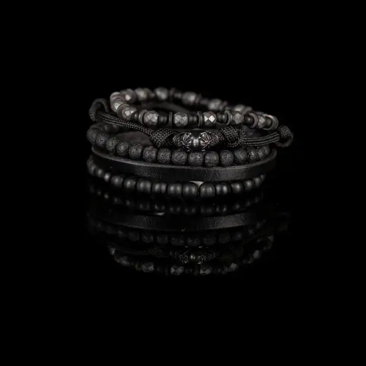 Black multi-layer men’s bracelet set featuring faceted hematite beads, matte black stones, lava stone accents, braided rope layers, and black leather strap detail on a light background.