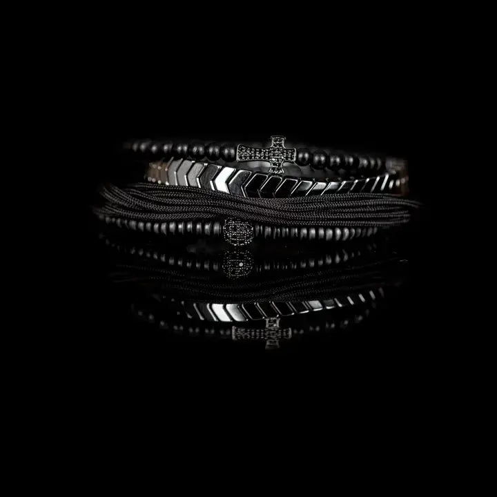 Black and silver layered men’s bracelet set with pavé cross detail, silver chevron metal strand, matte black beads, braided rope wraps, and pavé accent bead on white background.