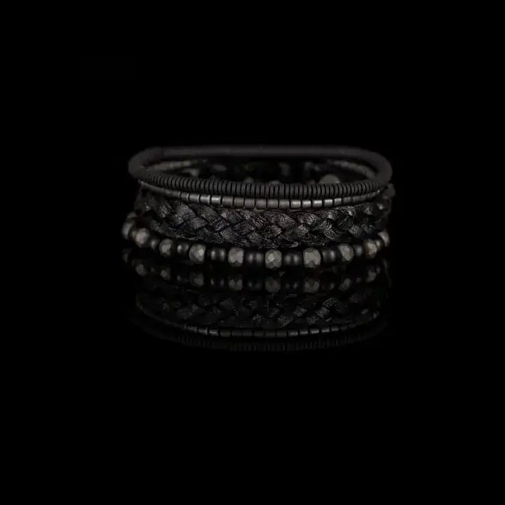 Black multi-layer men’s bracelet featuring braided leather, matte black onyx beads, faceted hematite stones, and layered metallic accents on a light background.