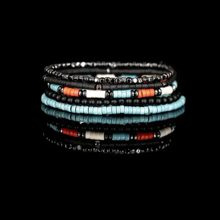Black multi-layer men’s bracelet featuring hematite cube bead strands, matte black onyx beads, turquoise disc beads, and orange accent details on a light background.