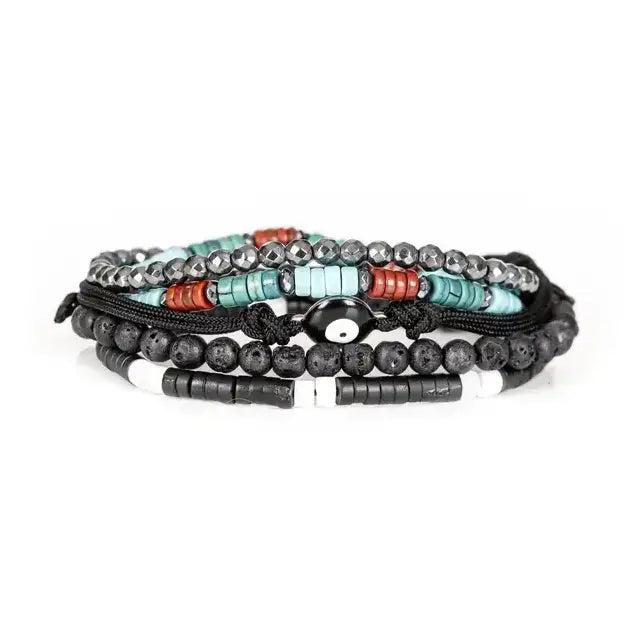 Men’s layered bracelet set featuring matte black lava stone beads, faceted hematite crystal beads, turquoise heishi beads, coral-red accent beads, black braided cord wraps, white and black spacer beads, and an evil eye centerpiece, stacked in a bold bohemian luxury design on a white background.