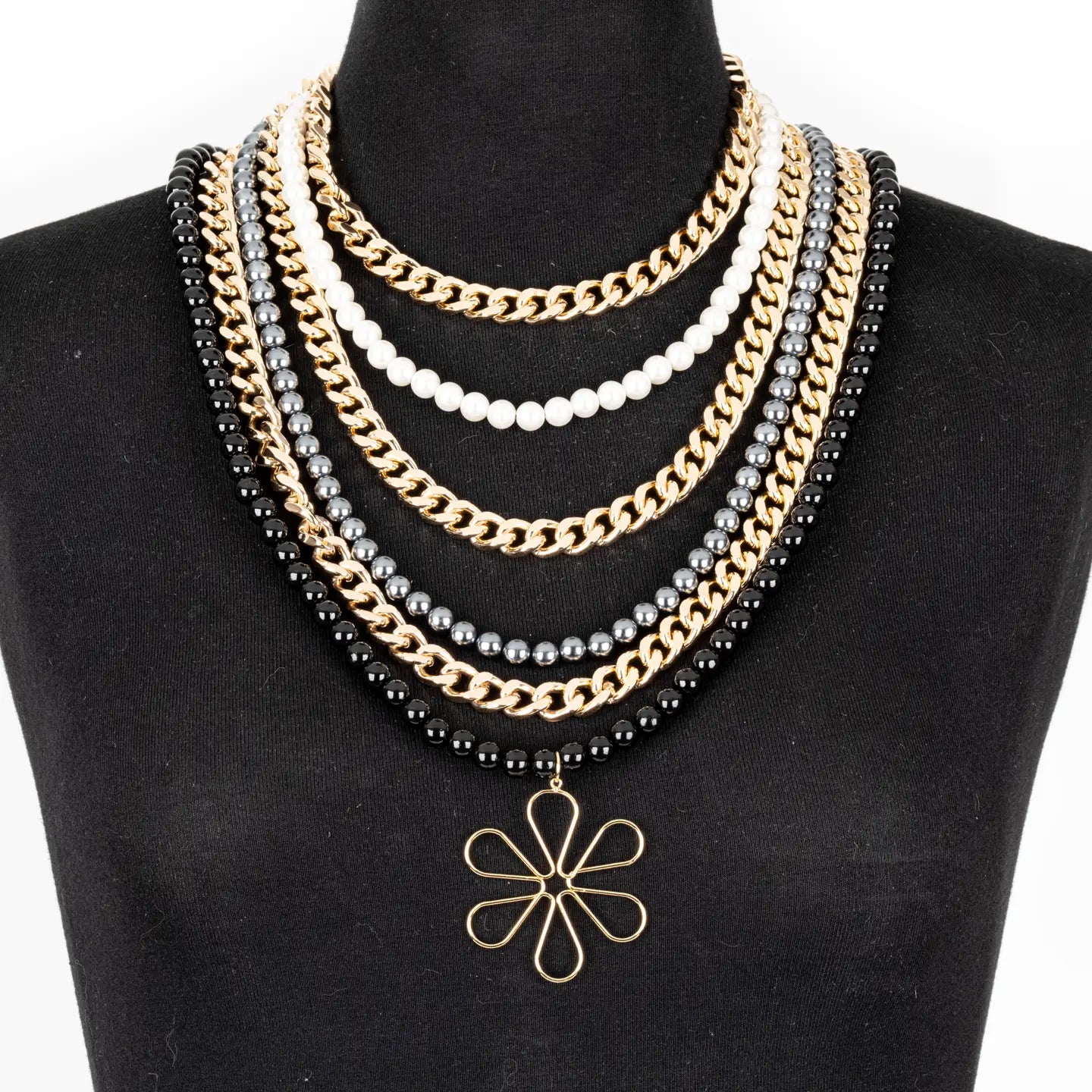 Multi-layer necklace with black, white, and metallic beads and chains, featuring a floral pendant, displayed on a white background.