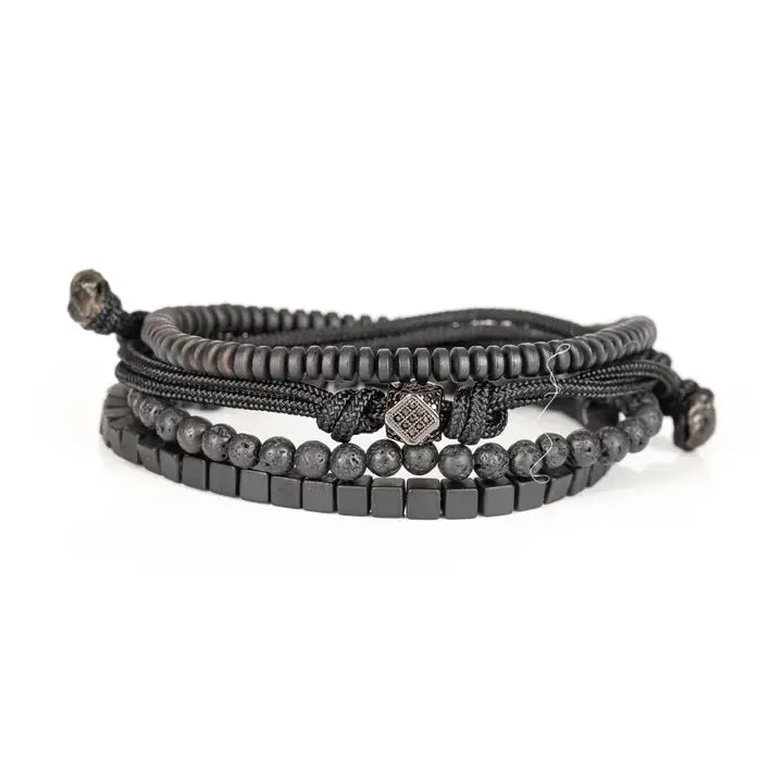 Black layered men’s bracelet set with lava stone beads, cube spacer beads, braided rope wraps, and pavé square centerpiece on white background.