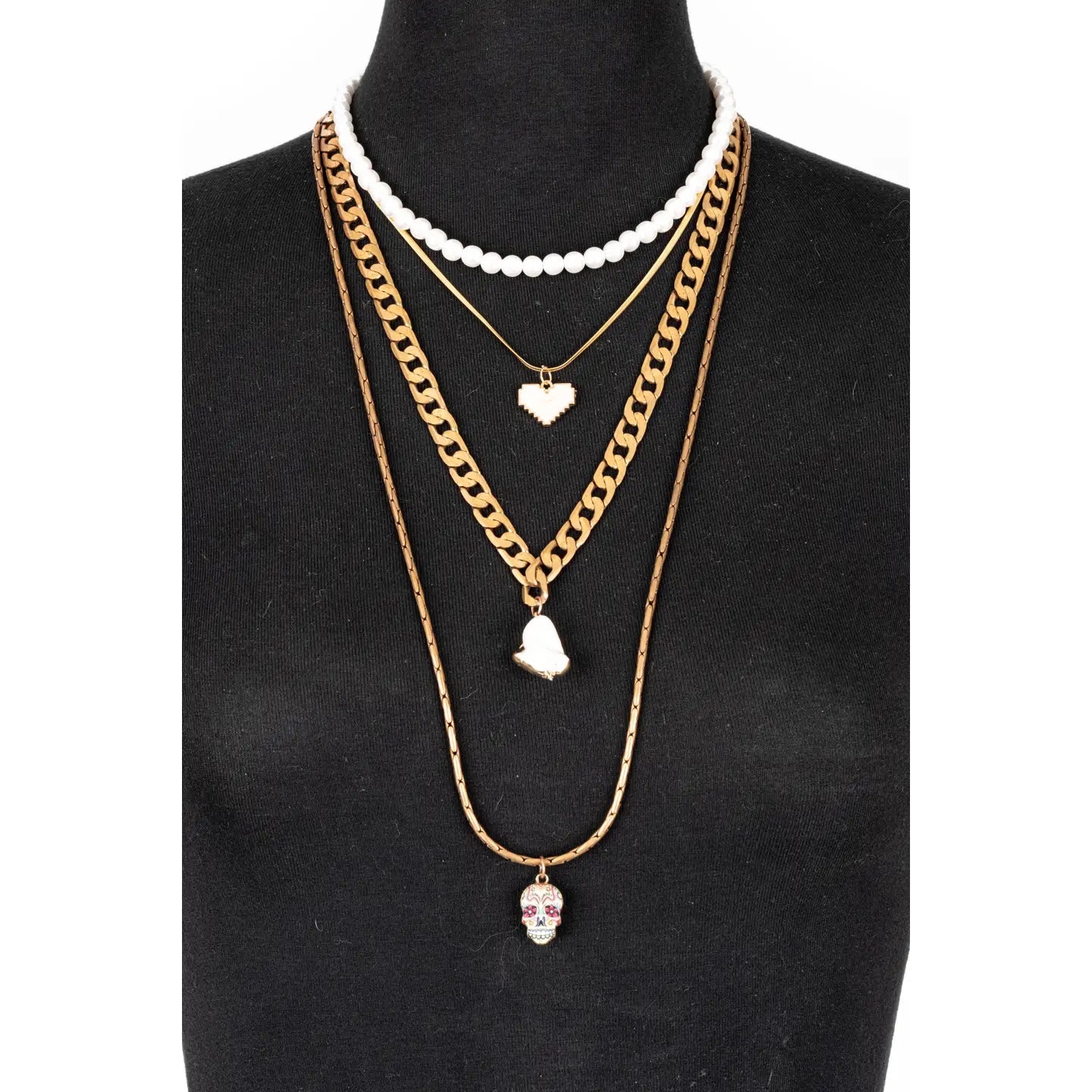 Layered gold necklace with white bead strand, heart charms, and skull pendant on white background.