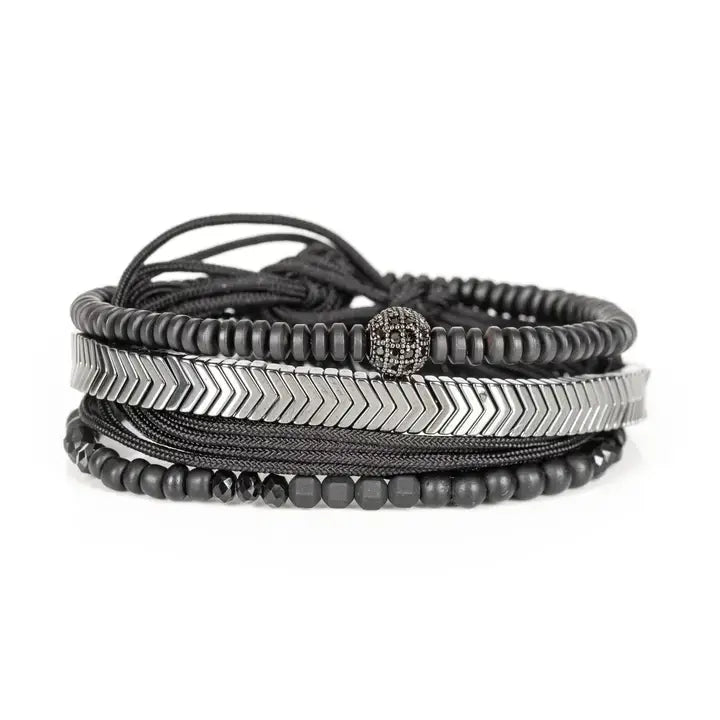 Black multi-layer men’s bracelet featuring silver chevron metal bar, hematite bead strands, crystal accent bead, faceted black stones, and braided black rope layers on a light background.