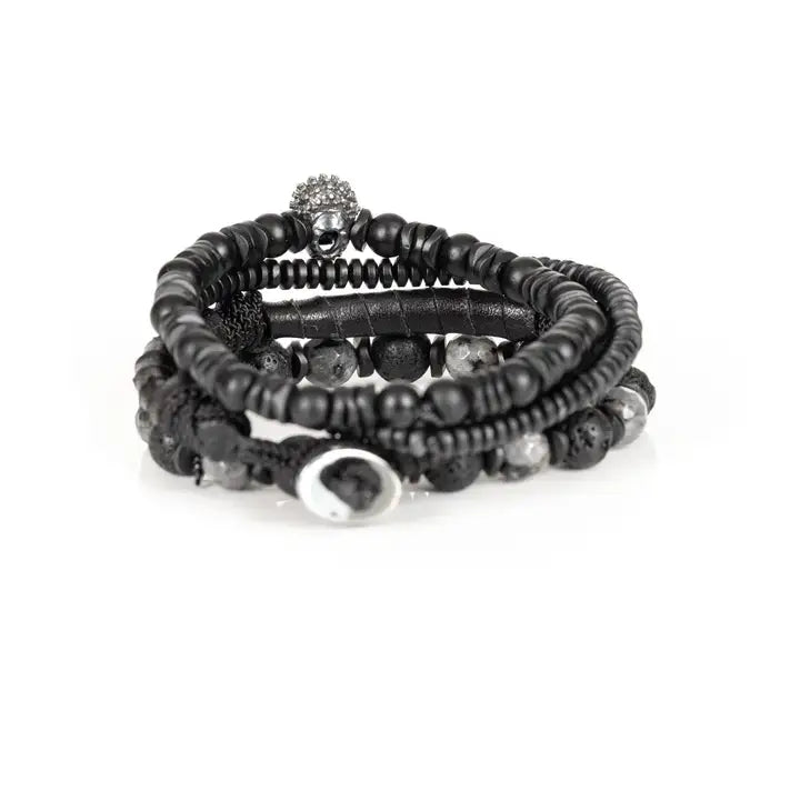 Black multi-layer men’s bracelet featuring crystal skull centerpiece, lava stone beads, marble grey natural stones, wrapped leather layer, and matte black bead strands on a light background.