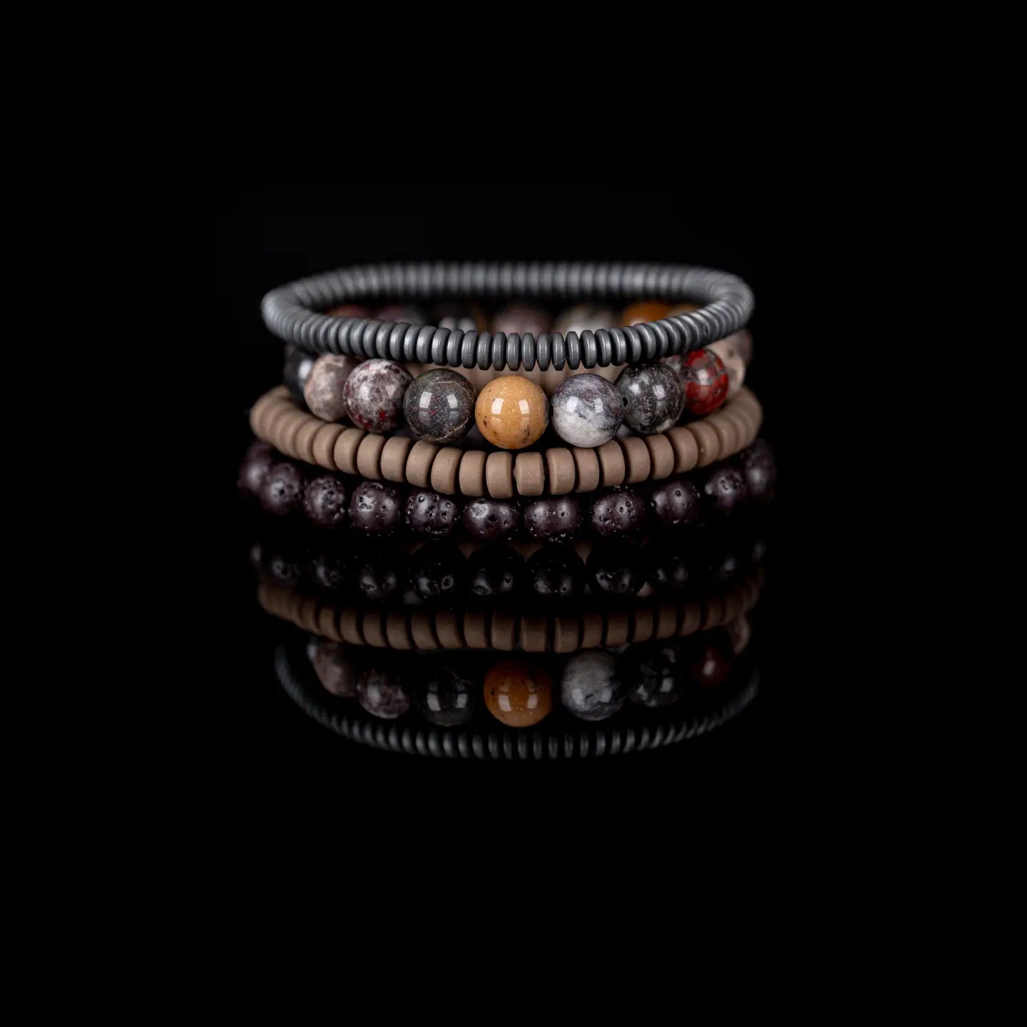 Men’s layered bracelet set featuring dark lava stone beads, multicolor natural stone beads in earthy brown, gray, cream, and rust tones, taupe heishi beads, and gunmetal coil wrap beads, stacked in a rugged natural luxury design on a white background.