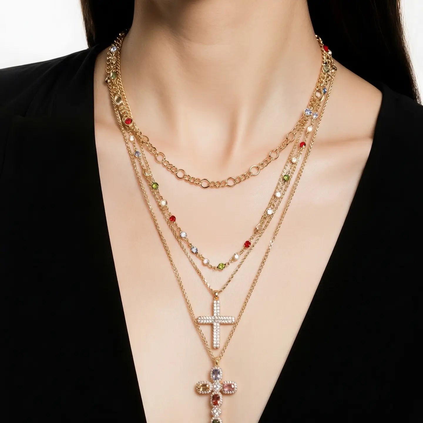 Layered gold necklace with multicolor stones and two cross pendants on a white background.