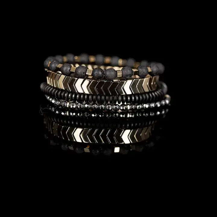 Men’s layered bracelet set featuring gold-tone chevron metal beads, matte black lava stone beads with gold-tone spacers, black heishi beads, and faceted hematite crystal beads, stacked in a sophisticated black and gold luxury design on a white background.