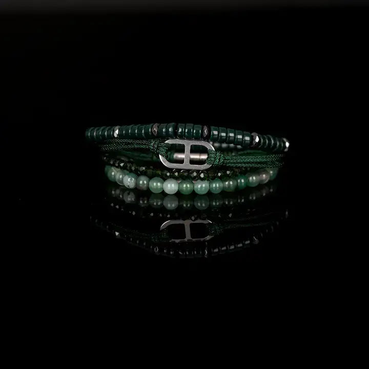Men’s layered bracelet set featuring dark green heishi beads, green braided cord with a silver-tone centerpiece, faceted green crystal beads, and polished green natural stone beads, stacked in a sophisticated contemporary luxury design on a white background.