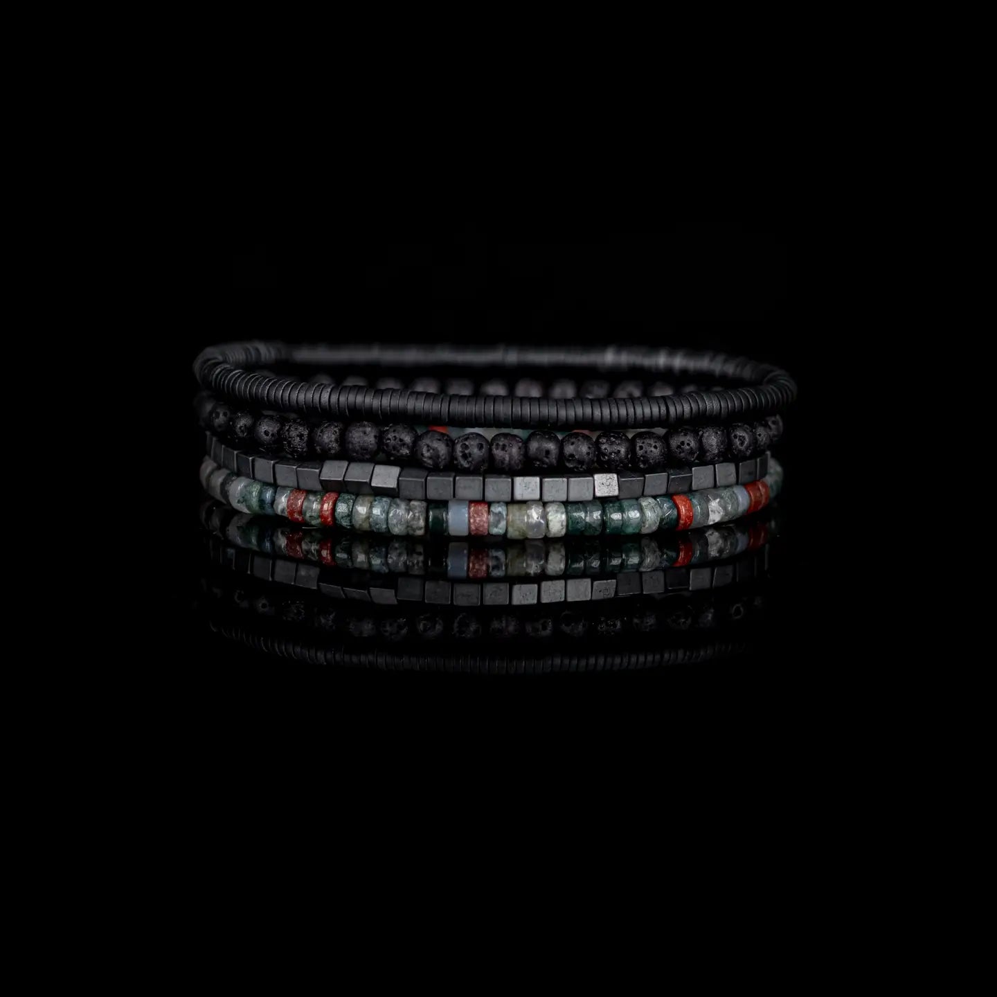 Men's layered bracelet set featuring matte black lava stone beads, hematite cube beads, and multi-color natural stone heishi beads in green, grey, and rust tones arranged in a stacked design on a white background.