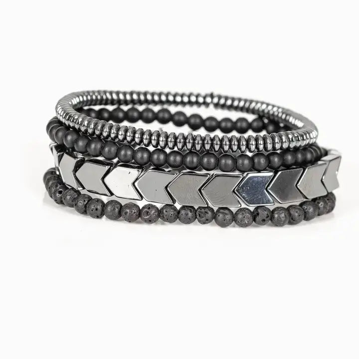 Men’s layered bracelet set featuring gunmetal chevron metal beads, matte black lava stone beads, black matte bead strands, and silver-tone hematite spacer beads, stacked in a bold industrial luxury design on a white background.