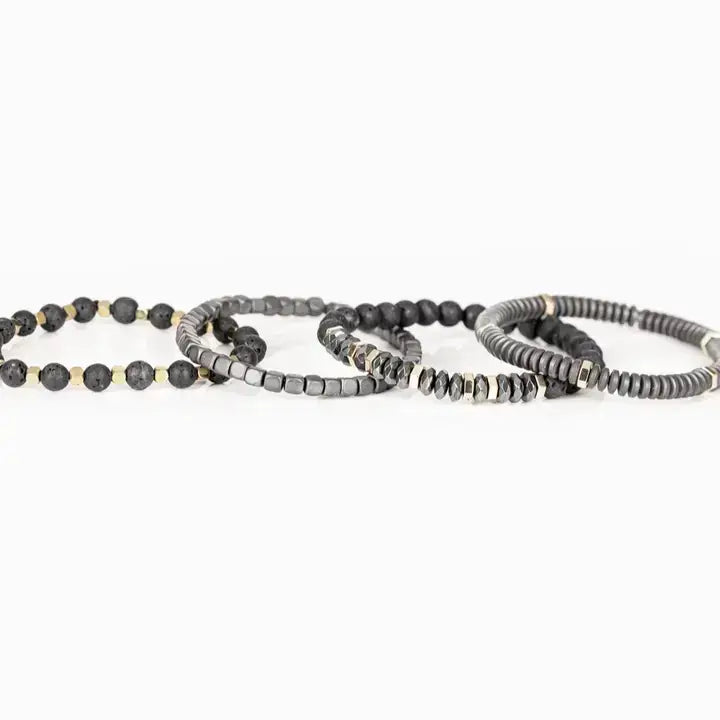 Men’s layered bracelet set featuring matte black lava stone beads, gray heishi beads, silver-tone hematite cube beads, faceted hematite crystal beads, and gold-tone spacer accents, stacked in a sophisticated industrial luxury design on a white background.