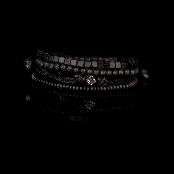 Black layered men’s bracelet set with lava stone beads, cube spacer beads, braided rope wraps, and pavé square centerpiece on white background.