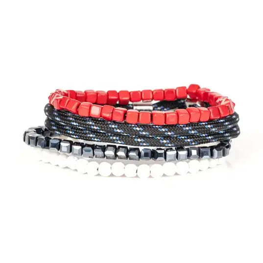 Men’s layered bracelet set featuring vibrant red cube beads, black braided cord with blue accents, faceted black hematite beads, and white heishi beads, stacked in a bold contemporary luxury design on a white background.