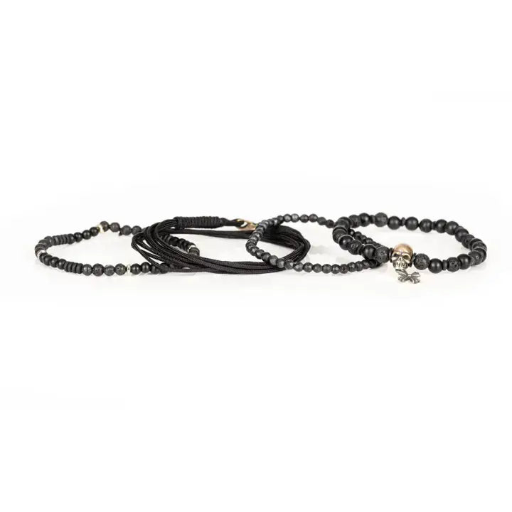 Black multi-layer men’s bracelet set featuring lava stone beads, matte onyx, faceted black stones, braided rope layers, metallic skull centerpiece, and cross accent on a light background.