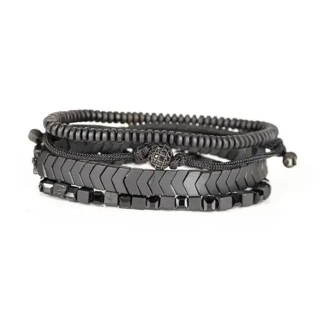 Men’s layered bracelet set featuring gunmetal chevron metal beads, black hematite cube beads, dark metallic heishi beads, black braided cord, and a pavé-style gunmetal accent bead, stacked in a sleek monochromatic luxury design on a white background.