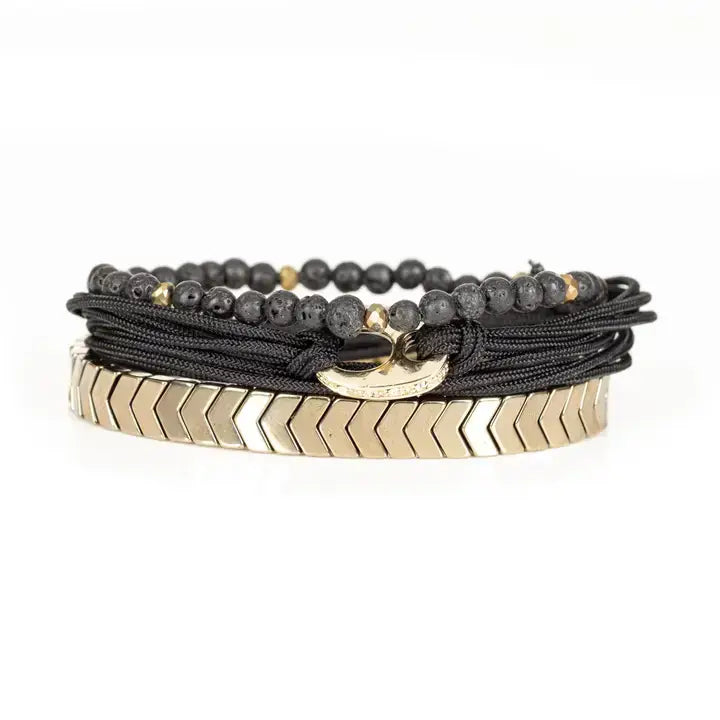 Black and gold layered men’s bracelet with lava stone beads, braided rope wraps, gold chevron metal bar, and metallic accents on white background.