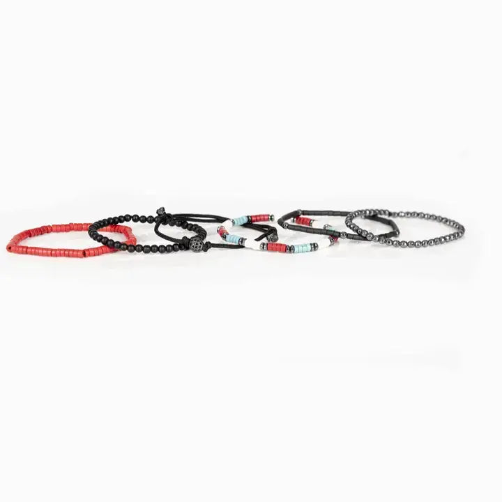 Men’s layered bracelet set featuring faceted hematite crystal beads, black heishi beads, turquoise and coral-red accent beads, matte black bead strands, black braided cord wraps, and a pavé-style gunmetal centerpiece, stacked in a bold contemporary bohemian luxury design on a white background.