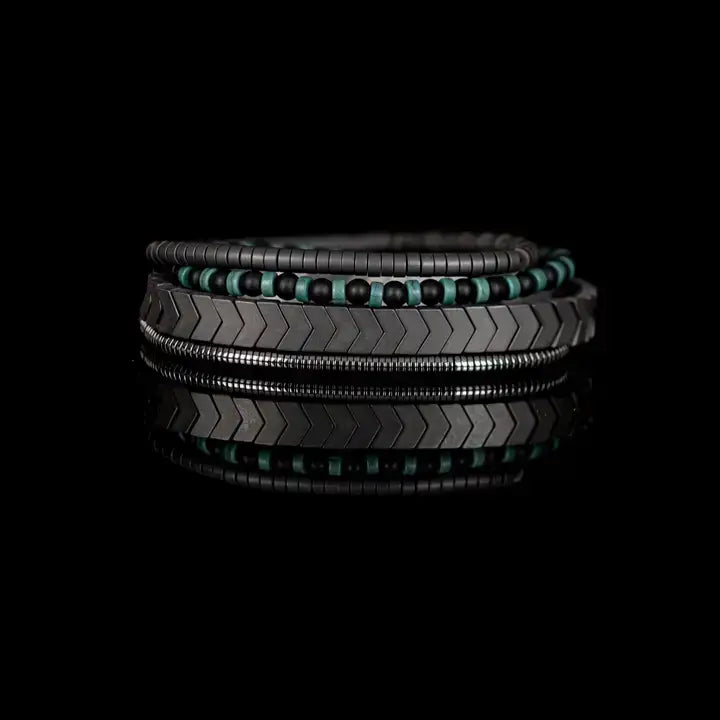 Men’s layered bracelet set featuring gunmetal chevron metal beads, black and turquoise beaded strands, dark hematite spacer beads, and silver-tone coil wrap accents, stacked in a modern industrial luxury design on a white background.