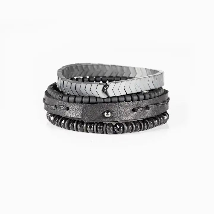 Men’s layered bracelet set featuring a silver-tone chevron stretch bracelet, black leather cuff with gunmetal stud details, matte black bead strand, and faceted black stone beads, stacked in a rugged contemporary luxury design on a white background.