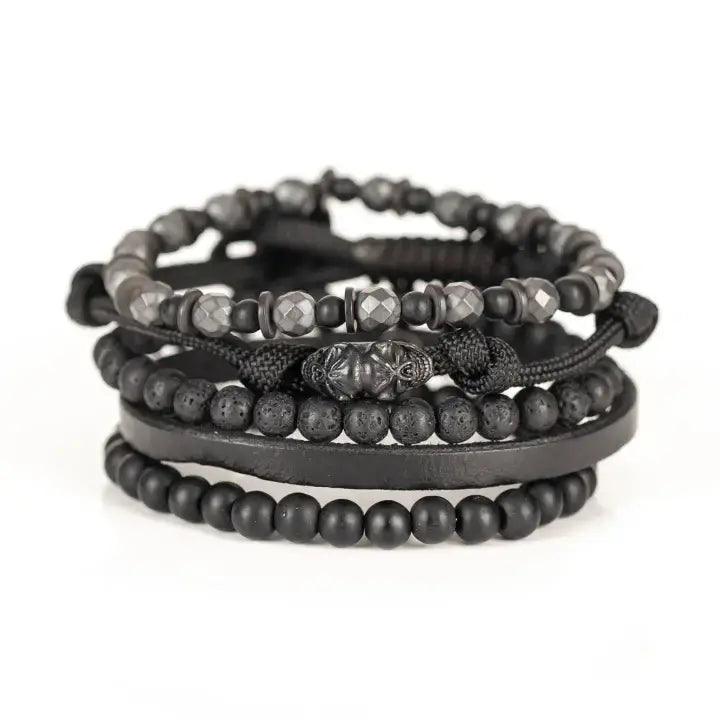 Black multi-layer men’s bracelet set featuring faceted hematite beads, matte black stones, lava stone accents, braided rope layers, and black leather strap detail on a light background.