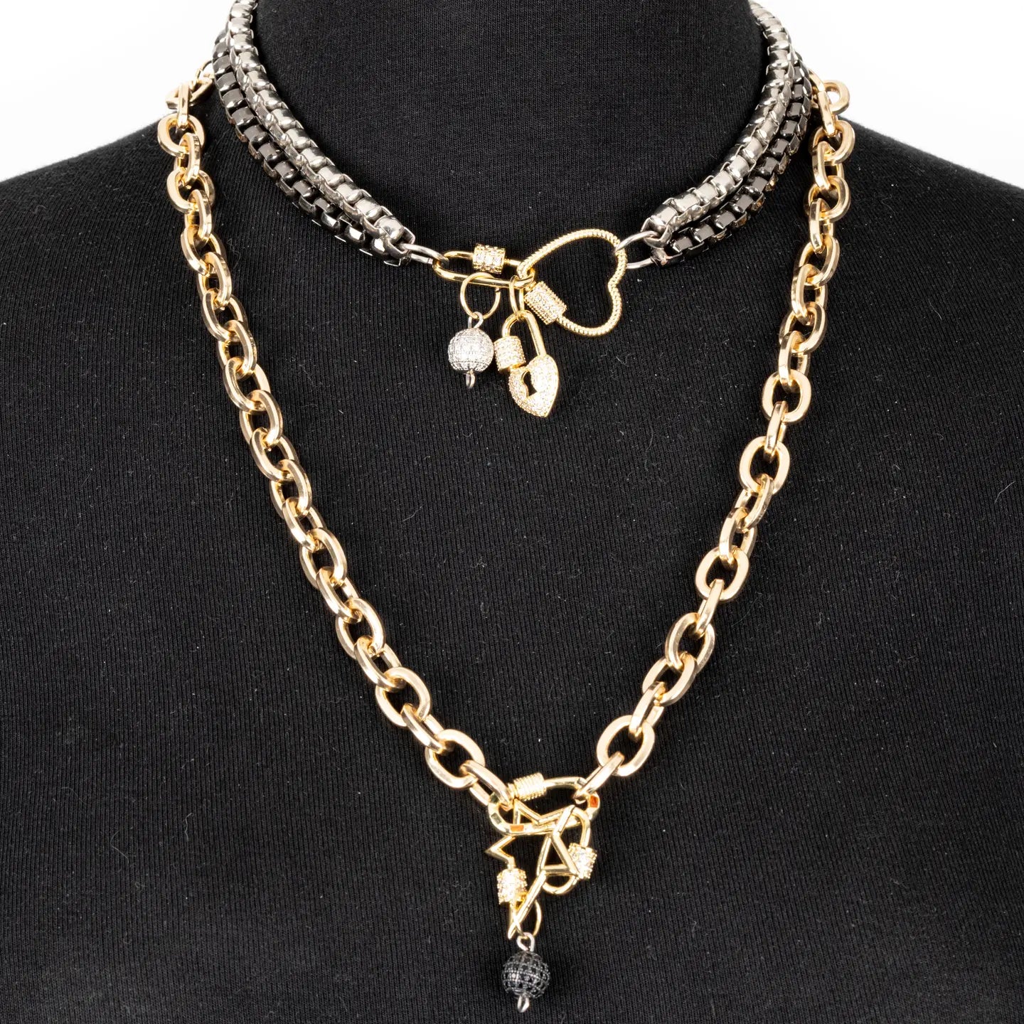 Mixed metal necklace with heart connector, charm details, and drop chain in gold and gunmetal tones on white background.