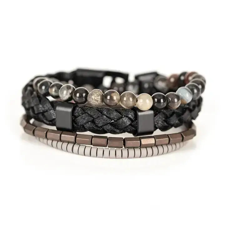 Black multi-layer men’s bracelet set featuring braided leather band, smoky grey natural stone beads, hematite cube accents, and layered metallic bead strands on a light background.