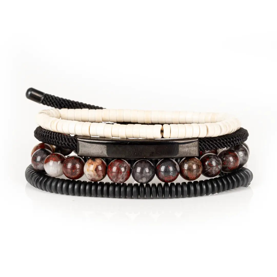 Men’s layered bracelet set featuring white howlite heishi beads, a gunmetal ID bar centerpiece, black braided cord wraps, red and black natural stone beads, and black coil wrap accents, stacked in a bold contemporary luxury design on a white background.