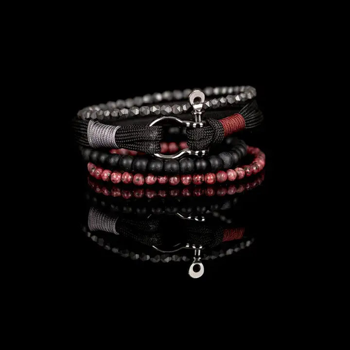 Black and red multi-layer men’s bracelet featuring metallic hook clasp, braided black rope, faceted hematite crystals, matte black beads, and red marbled natural stone beads on a light background.